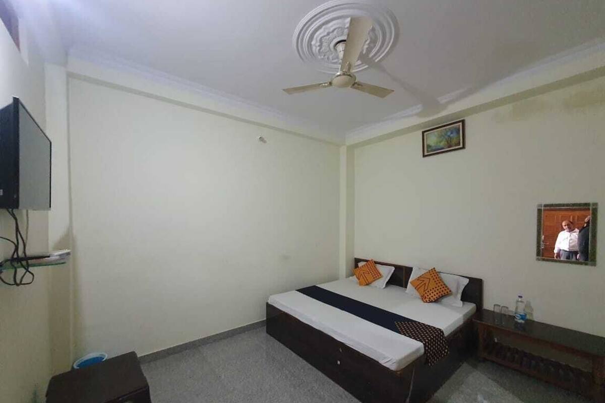Un dormitorio con una cama, ventilador de techo, televisor en la pared y una mesita.