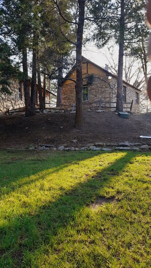 A stone house with a stone exterior, surrounded by trees and a grassy area. - SHERWOOD ARMS MOTEL_CABIN #2 (Running Springs)