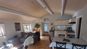 A spacious living area with a sofa, dining table, and chairs, a kitchen with cabinets and appliances, and a ceiling with exposed beams. - Renovated chalet located by the Ourthe. (Tohogne)