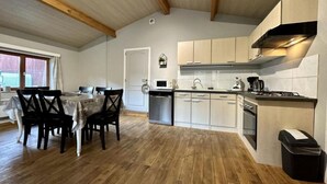 A modern kitchen with wooden beams, a dining area with a table and chairs, and a view of the outside. - Renovated chalet located by the Ourthe. (Tohogne)