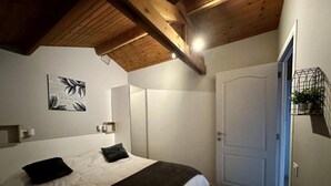 A bedroom with a large bed, a wooden ceiling, a white door, and a small plant on the wall. - Renovated chalet located by the Ourthe. (Tohogne)