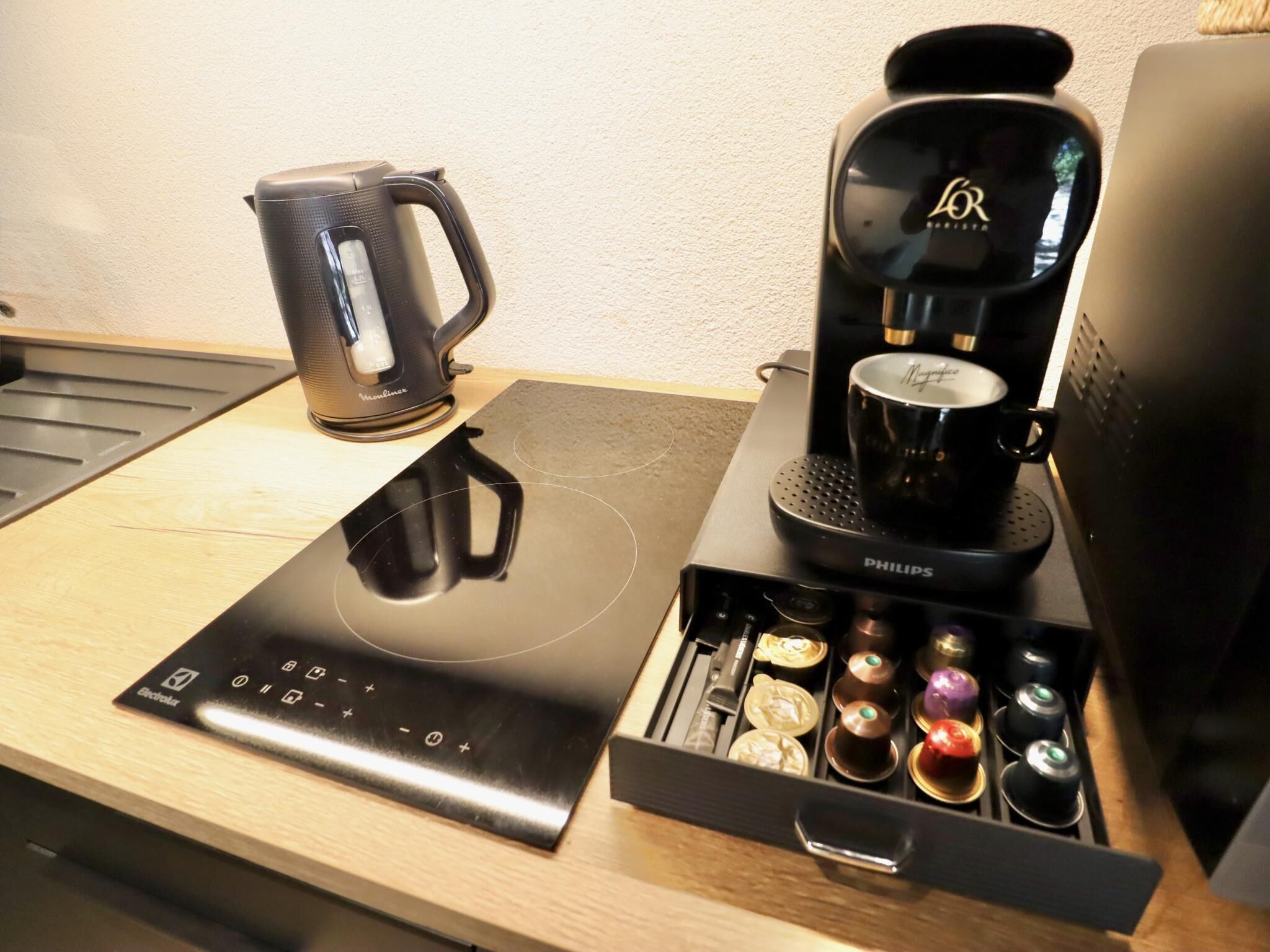 Una cafetera, un hervidor y un soporte para cápsulas de café sobre una encimera de madera.