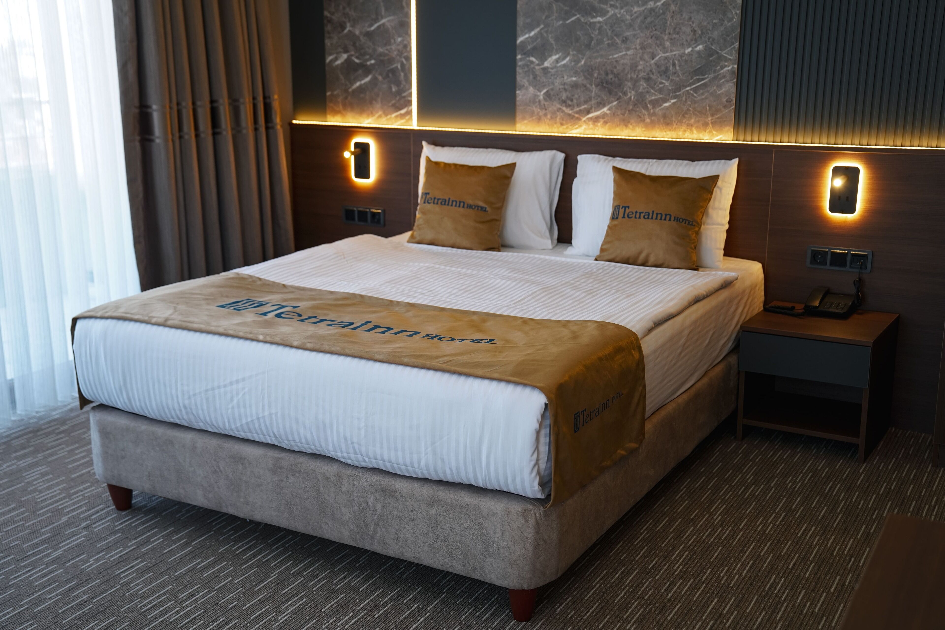 A hotel room with a large bed, a nightstand, and a wall-mounted phone.