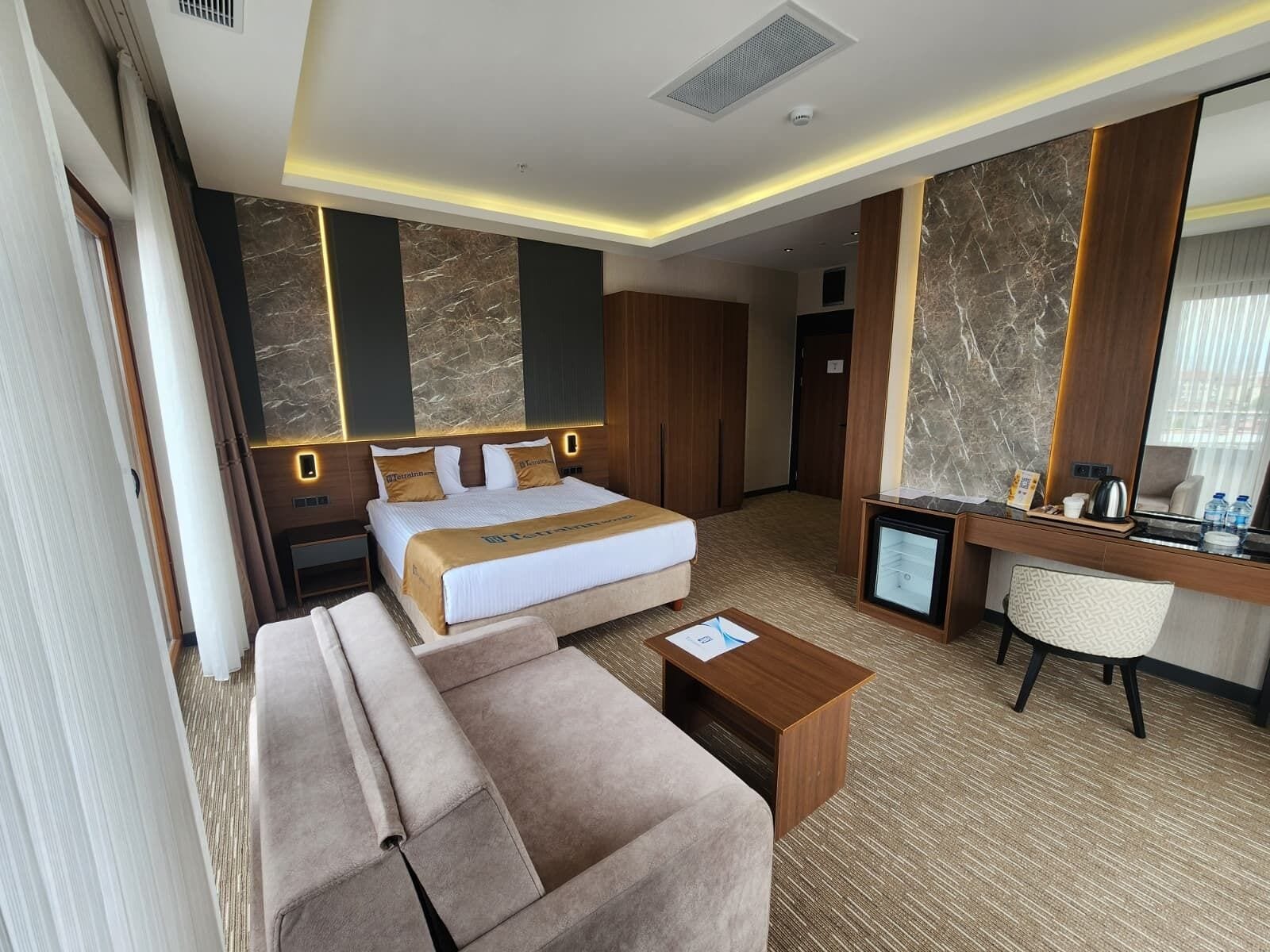 A hotel room with a bed, a sofa, a desk, a chair, and a small TV.