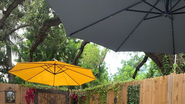 Eine Terrasse mit einem Korbsessel, einem gelben Sonnenschirm und einem blauen Teppich mit Muster.
