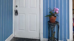 Eine weiße Tür mit einem Zahlenschloss, eine blau-weiß gestreifte Wand, ein Schild mit Tulpen und eine Orchidee in einem Topf auf einem Metalltisch.