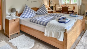 Un dormitorio con una cama de madera, almohadillas estampadas en cuadros, una mesita de noche con una lámpara y un reloj de pared.