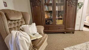 Un sillón cómodo con un libro, un aparador de madera con puertas de cristal y un suelo alfombrado.