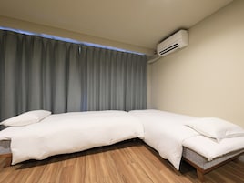 Una cama individual con estructura de madera y cabecera gris, una cortina gris y un equipo de aire acondicionado montado en la pared.