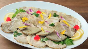 Un piatto bianco con fette di carne guarnito con prezzemolo, fette di limone e fiori eduli.