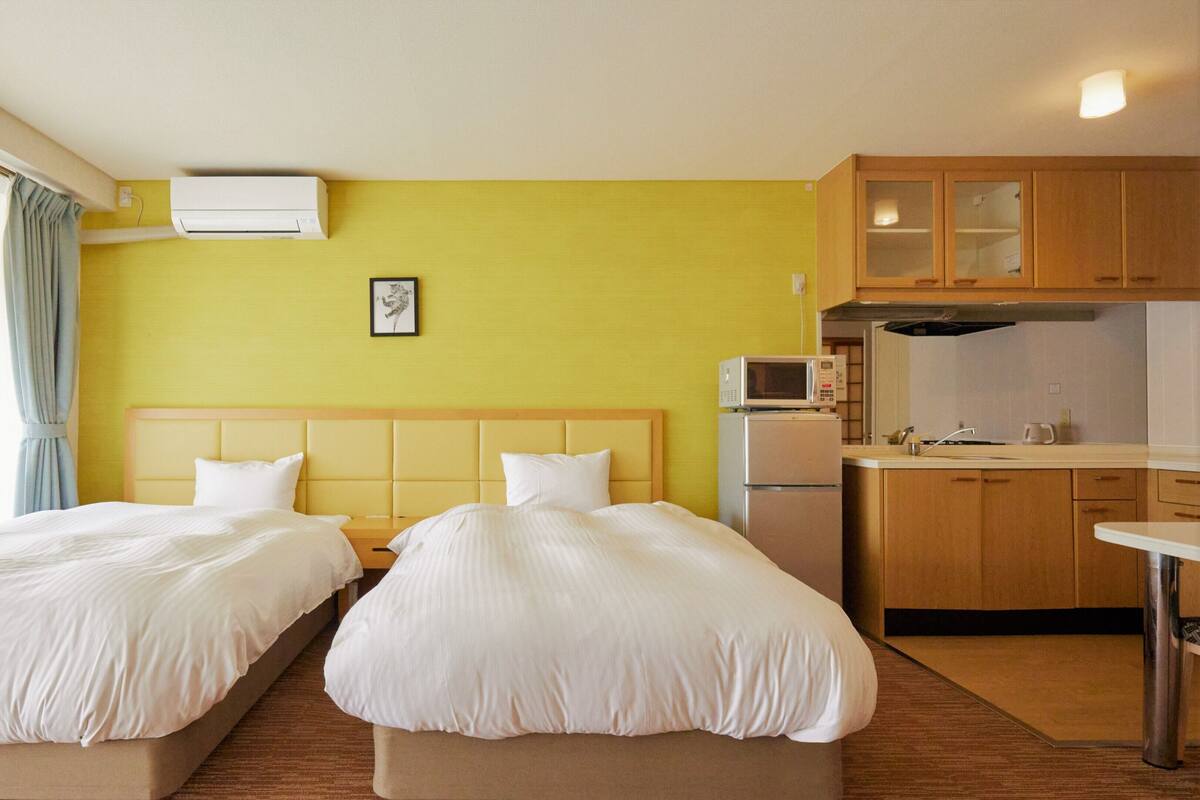 Una camera d'albergo con due letti, angolo cottura e finestra con tende.