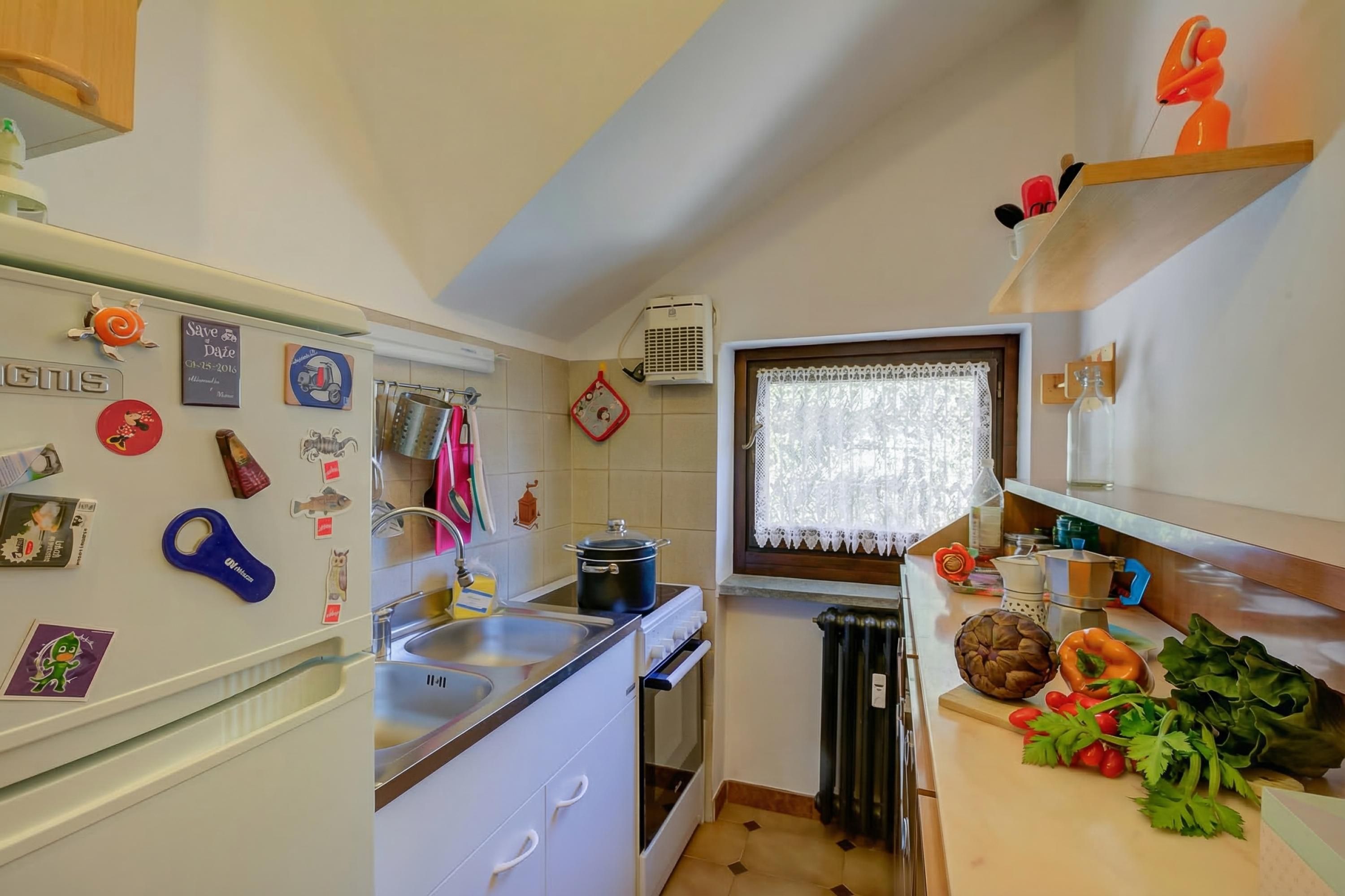 Una cocina compacta con un lavamanos, estufa y ventana con cortinas de encaje.