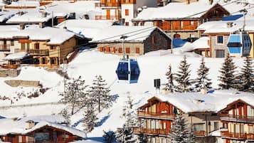 Un pueblo en la montaña cubierto de nieve con edificios de madera, un telesilla y pinos.