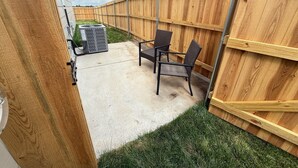 Een terras met een betonnen vloer, een houten omheining en twee rieten stoelen.