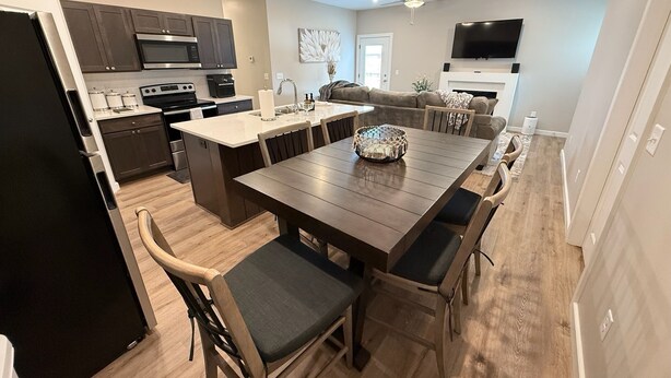 Een moderne keuken met donkere kastjes, een centraal eiland en een eethoek met houten tafels en stoelen.