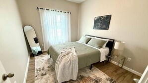 Een slaapkamer met een bed, een nachtkastje met lamp, een spiegel en een kunstwerk aan de muur.