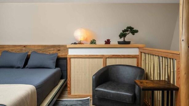 Una habitación con una cama, una silla, una mesita, un estante con adornos y una lámpara.