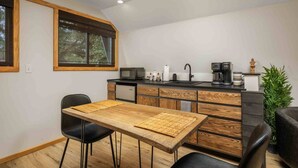 Cocina pequeña con una mesa de madera, sillas negras y una cafetera.