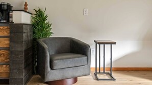 Una sala de estar moderna con un sillón de cuero oscuro, una mesita de madera pequeña, una planta alta y una cafetera integrada.