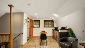 Cocina compacta con zona de comedor, suelo de madera y una silla negra.