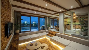 Un soggiorno moderno con pavimento in legno, sedute integrate e ampie finestre che si affacciano su una piscina.