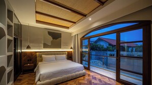 Una camera da letto moderna con un letto grande, pavimento in legno e vista su un quartiere residenziale attraverso ampie finestre.