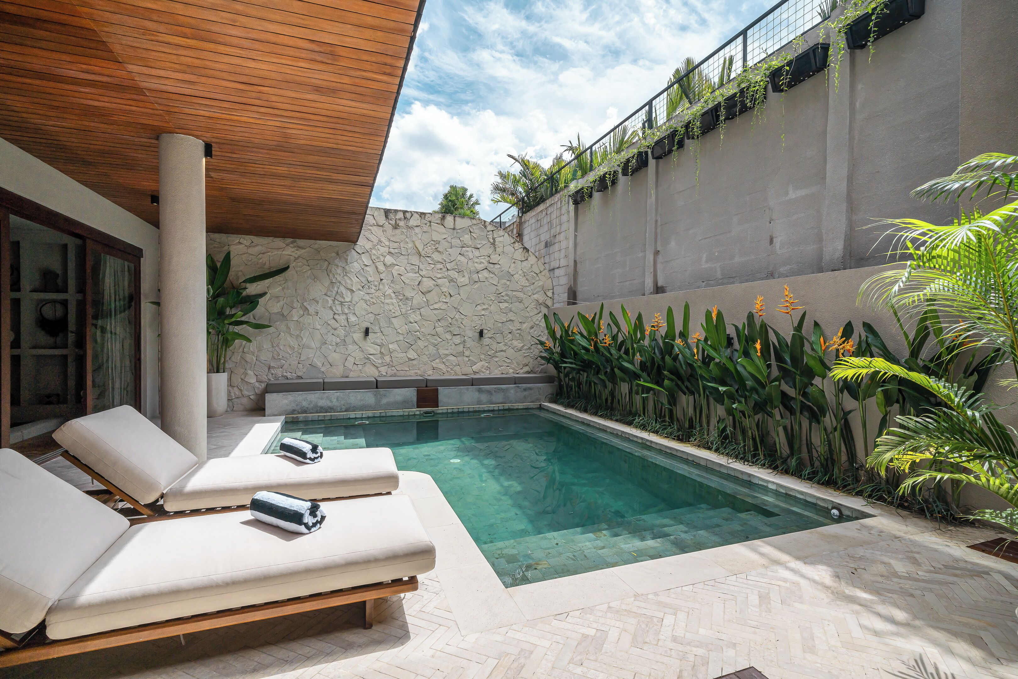 A modern outdoor pool area with lounge chairs and a stone wall.