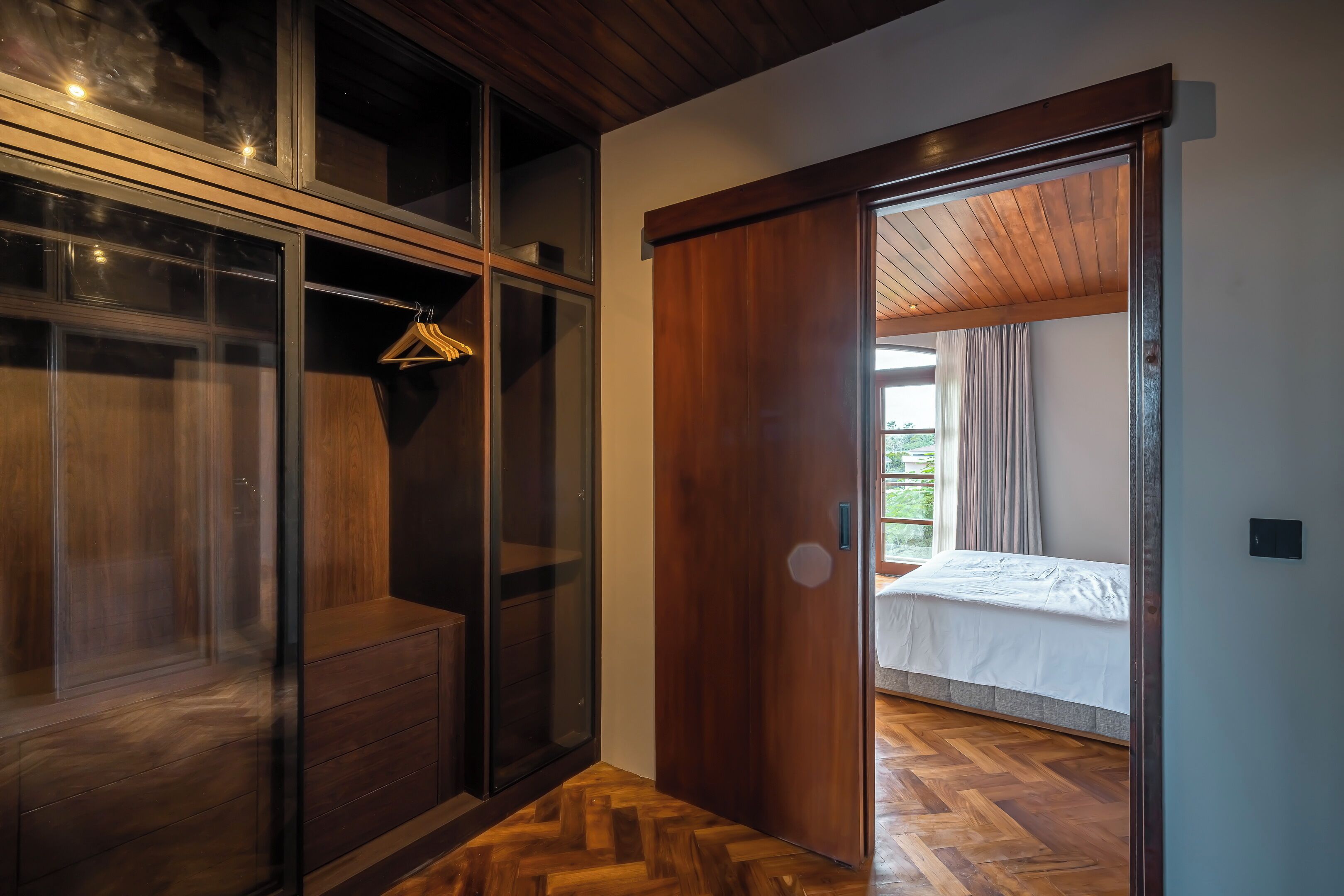A bedroom with a wooden floor, a bed, and a sliding door leading to a balcony.