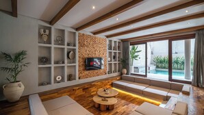 Un soggiorno moderno con pavimento in legno, scaffali a muro, una TV e un’area salotto con vista su una piscina.