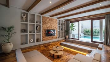 Una sala de estar moderna con piso de madera, estanterías empotradas, televisor y una zona de estar con vista a una piscina.