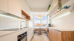 A modern kitchen with a central island, built-in oven, and a view through a large window.