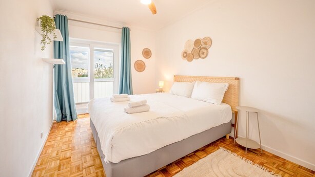 A bedroom with a bed, a ceiling fan, a window with curtains, and a view of the outside.