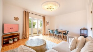 A spacious living room with a TV, a dining area, and a large window with curtains.