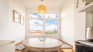 A modern kitchen with a round table, a hanging light fixture, a view of the city through large windows, and a built-in oven.