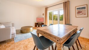 A dining area with a wooden table and chairs, a sofa, and a television on a stand.