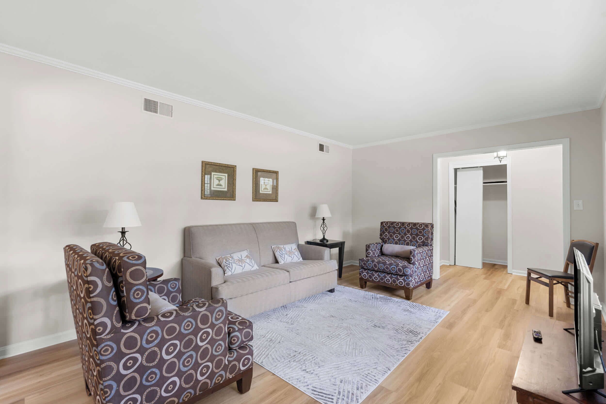 A living room with a sofa, armchair, and patterned armchair, a flat-screen TV, and a coffee table.