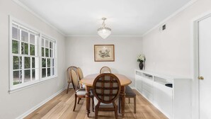 A dining room with a round table, four chairs, a chandelier, a framed picture on the wall, and a white cabinet with a vase of flowers. - Southern haven - family retreat (Statesboro)