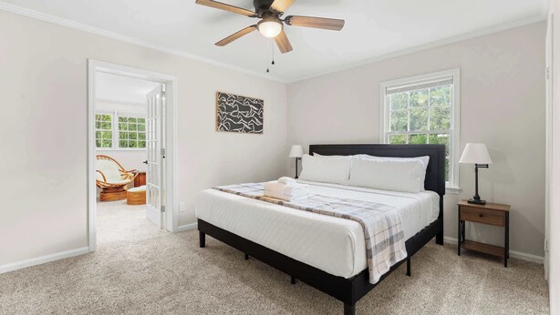 A bedroom with a bed, a ceiling fan, a nightstand, a window, and a door leading to another room. - Southern haven - family retreat (Statesboro)