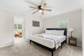 Ein Schlafzimmer mit einem Bett, einem Deckenventilator, einem Nachttisch, einem Fenster und einer Tür zu einem anderen Raum.