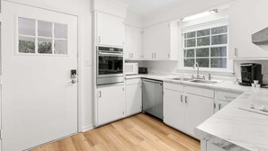 A modern kitchen with white cabinetry, a built-in oven, a dishwasher, and a large window providing natural light. - Southern haven - family retreat (Statesboro)