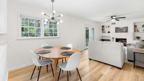 A modern living room with a round wooden table, white chairs, a grey sofa, and a ceiling fan. - Southern haven - family retreat (Statesboro)