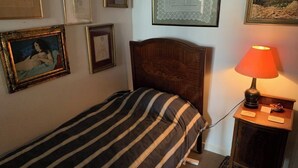 A single bed with a striped bedspread, a wooden headboard, a nightstand with a lamp, and framed artwork on the walls.