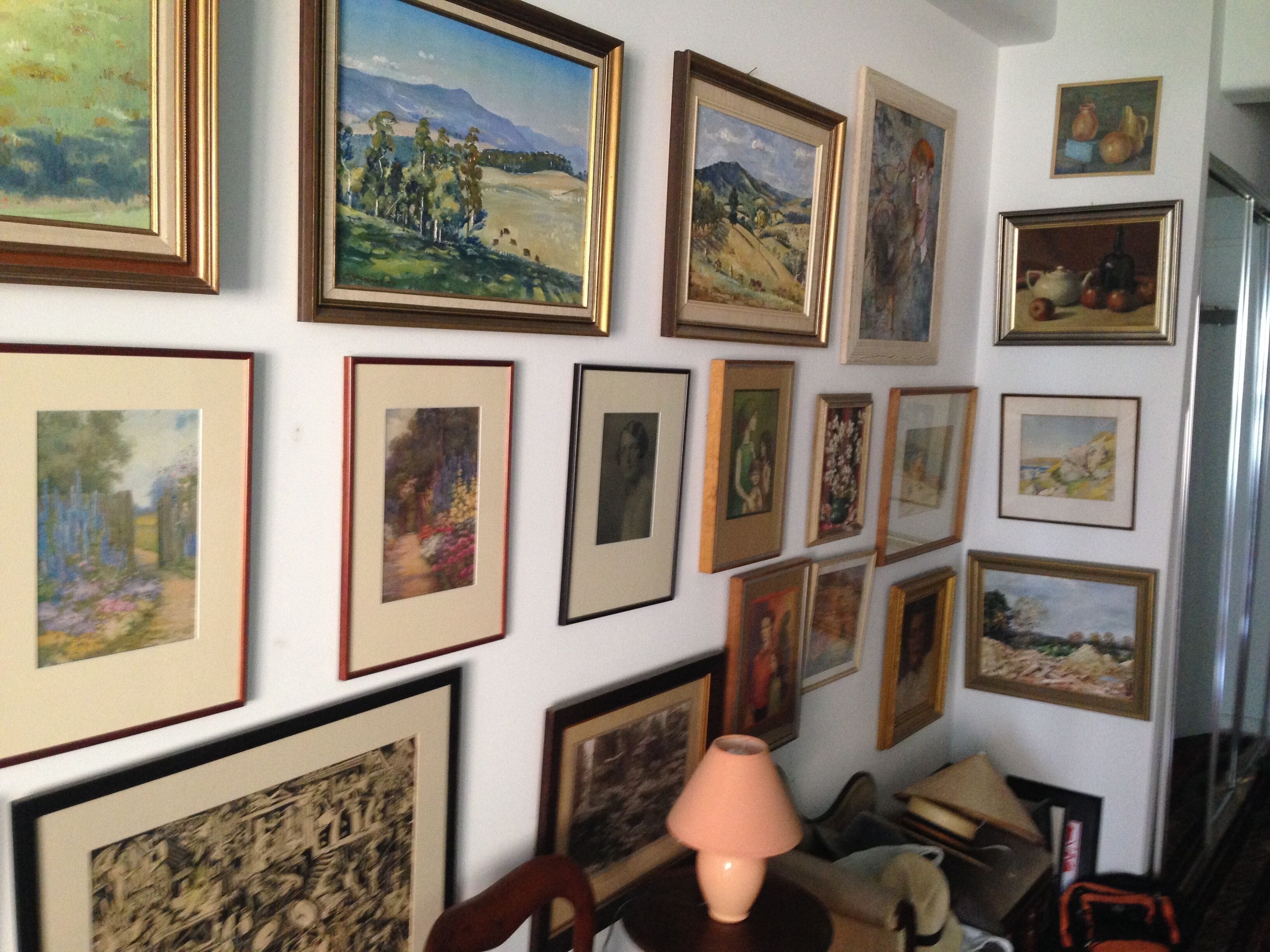 A wall with multiple framed artworks, a lamp, and a chair.