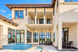 A two-story house with a swimming pool, outdoor seating, and large windows.
