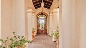 Un pasillo con puerta de madera, columnas y plantas en macetas.