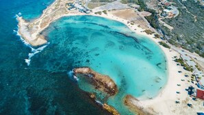 Vista aérea de una zona costera con una playa arenosa, aguas azul turquesa y una pequeña península.