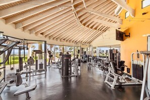 Une salle de sport équipée de divers appareils d’exercice, dotée d’un plafond en bois et de grandes fenêtres offrant une vue sur l’extérieur.