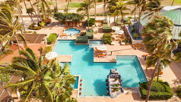 Un resort con varias piscinas, palmeras y zonas de descanso.
