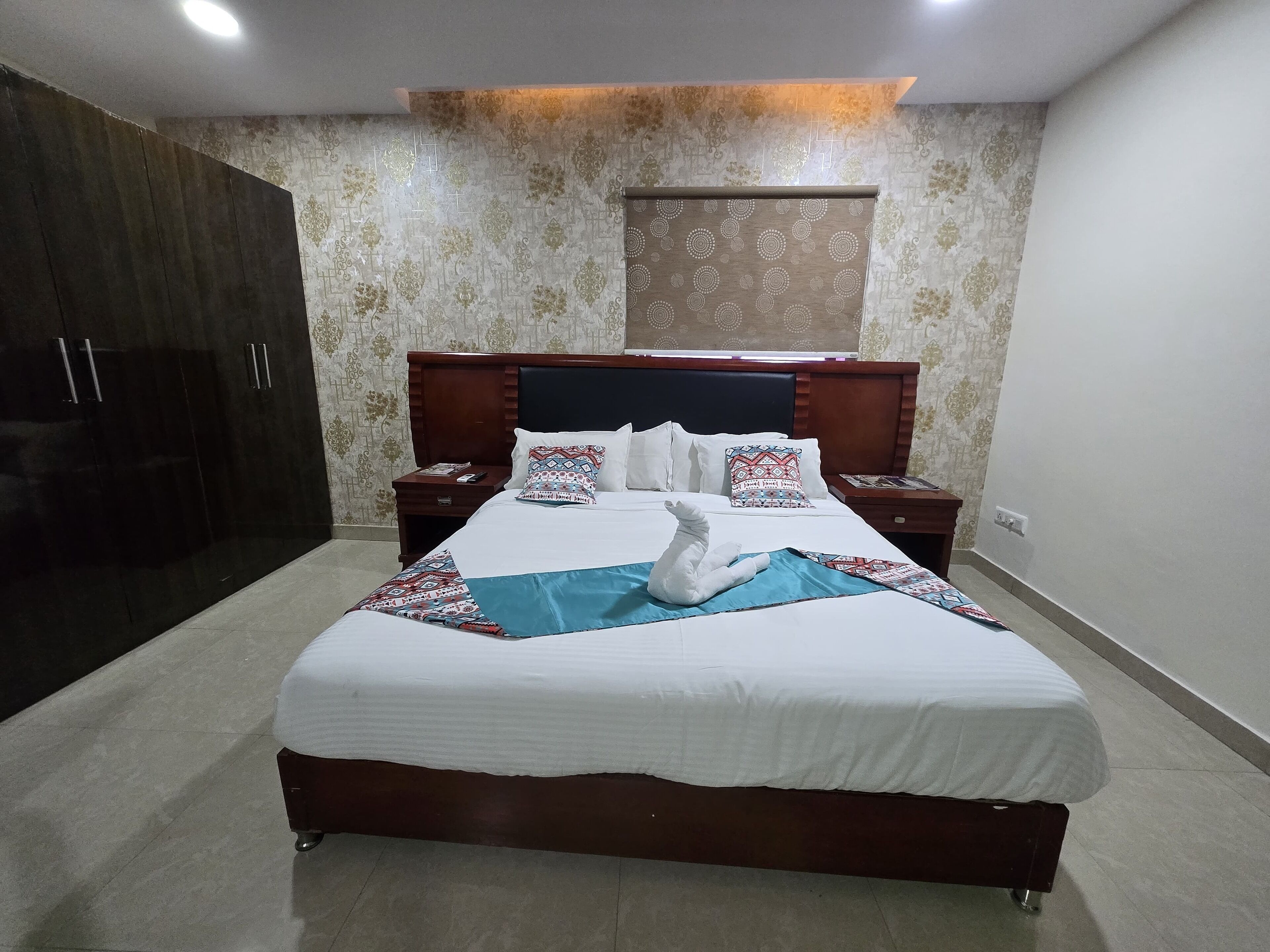 A neatly made bed with a white comforter and patterned pillows, a wooden headboard, and a bedside table with a remote control.