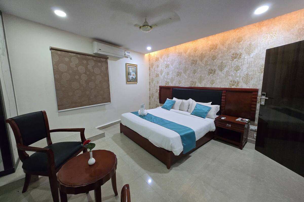 A hotel room with a bed, bedside table, chair, and a small table with a vase.